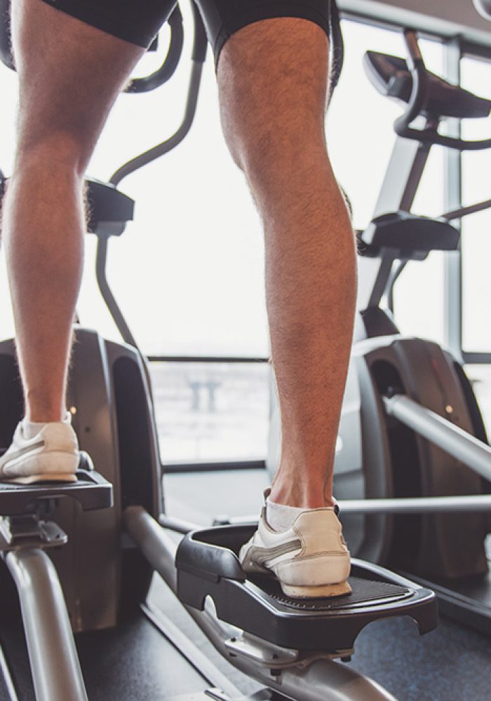 Back view of attractive young people working out on an elliptical trainer in gym